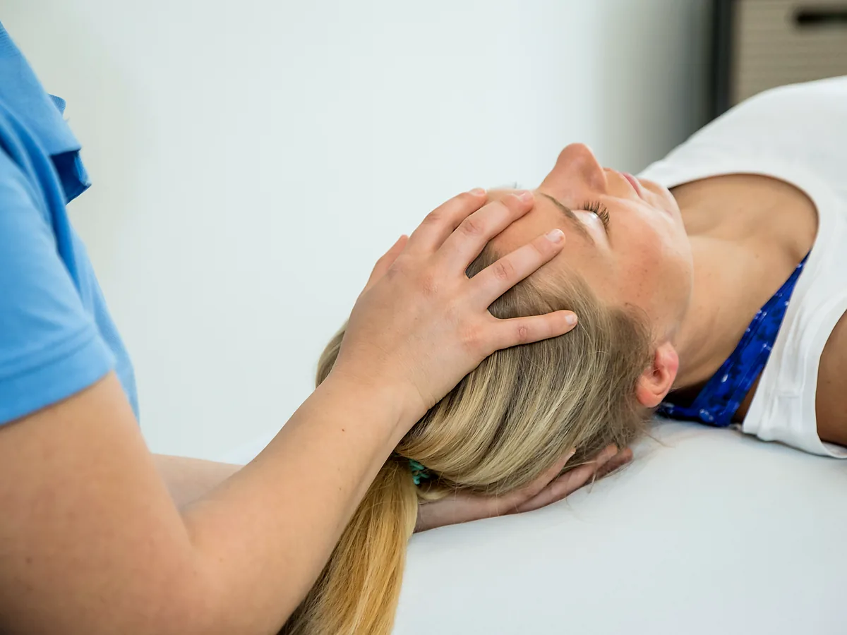 Physiotherapeutin behandelt den Nacken einer liegenden Patientin